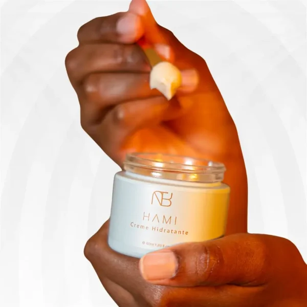 Mão segurando frasco aberto do HAMI Creme Hidratante da Nutri Bu Alma, com espátula a retirar o produto.